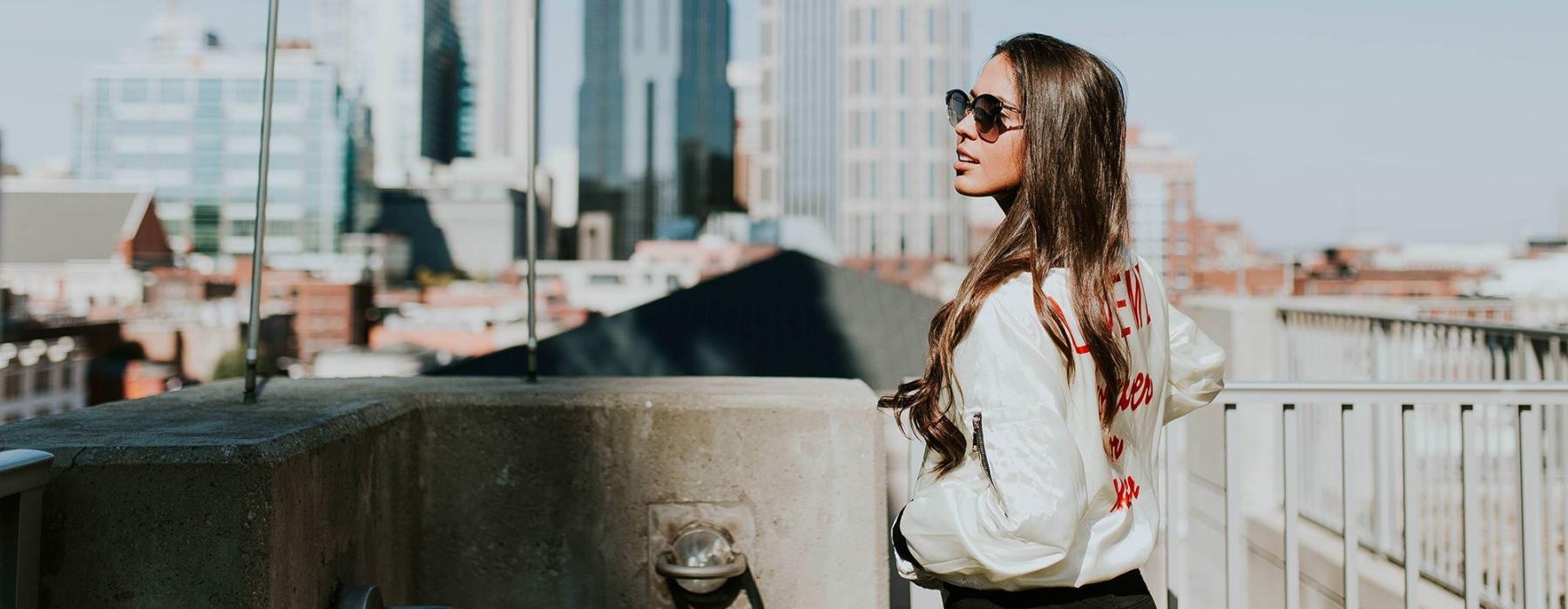 woman with sunglasses stands on a rooftop overlooking the city